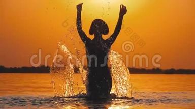 日落时的女人剪影举起双手，创造水的飞溅。 慢动作