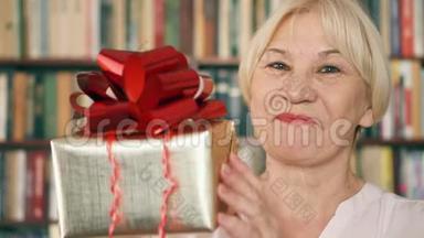 有礼物的高级女人。 领取养老金的人拿着红色丝带的金色礼盒庆祝生日