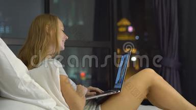 一位年轻<strong>女士</strong>正在用笔记本电脑交谈，她坐在床上，背着一个背景的摩天轮<strong>剪影</strong>