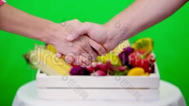 <strong>特写</strong>，友好的<strong>握手</strong>在Chromakey，绿色背景和一个盒子充满不同的蔬菜，在工作室。 概念