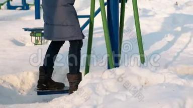 在城市的冬季公园里，特写女子腿从事滑雪模拟器。 雪花飘来飘去。