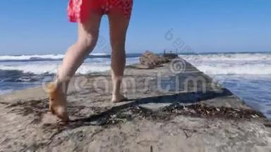 年轻女子的腿赤脚行走在码头上，强烈的波浪撞击码头。