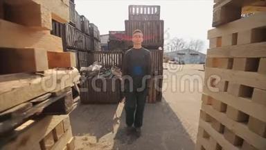 一位穿制服的年轻工人在配电室外仓库的木托盘之间行走。 慢动作