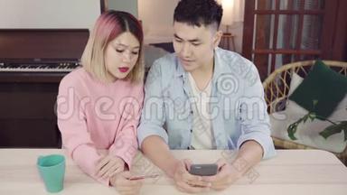 年轻的亚洲<strong>家</strong>庭夫妇使用智能手机讨论新闻或做网上购物一起坐在办公桌上的<strong>家</strong>庭<strong>周末</strong>。