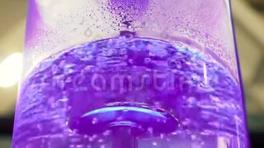 用霓虹灯背光和金属管在大型玻璃冷却器中沸腾水。 媒体。 冷却器中最纯净水的特写镜头