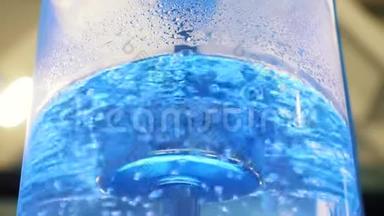 用霓虹灯背光和金属管在大型玻璃冷却器中沸腾水。 媒体。 冷却器中最纯净水的特写镜头