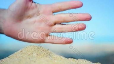 手特写放沙.. 沙子在蓝色的海洋上流过。 暑假海滩度假。
