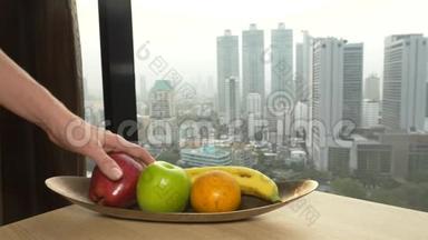 手把苹果从盘子里拿出来，靠在窗户上，看着摩天大楼。 4k，慢动作