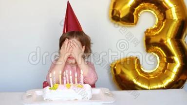 有趣的快乐孩子许愿，在聚会上吹灭生日蛋糕上的蜡烛。 可爱的小女孩戴着粉红色的帽子微笑着