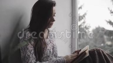 漂亮的小姐坐在房子的窗台上看书。 大窗户，绿植..