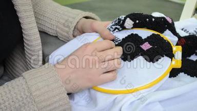 这位女士用手在白色织物上绣着乌克兰刺绣，在正确的角度上用黑色的羊毛线刺绣