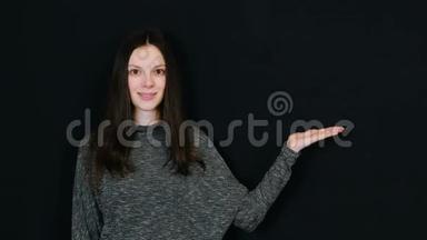 微笑的黑发女人向右<strong>展示</strong>手掌，在黑色背景下看并<strong>展示</strong>。 提供文本的房间。