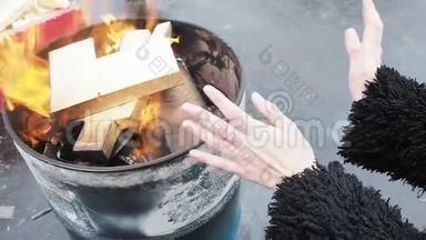 女人在燃烧的壁炉前搓手。 女孩正在温暖自己在冬天的火在一个圆桶