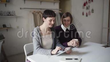 <strong>两个</strong>姐妹用平板<strong>电脑</strong>坐在家里的桌子上。 女人喜欢平板<strong>电脑</strong>