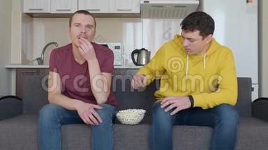 两个男人坐在沙发上看电视上的<strong>足球赛</strong>，吃着爆米花