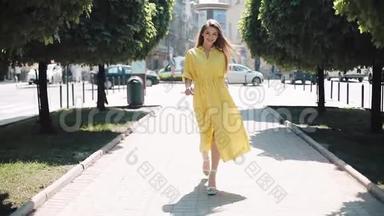 美丽的女孩穿着黄色的裙子沿着街道的城市走。 背景模糊<strong>阳光</strong>明媚的夏日<strong>阳光</strong>女子