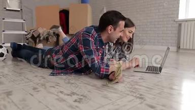 一对穿格子衬衫的幸福夫妇躺在一间新公寓的地板上，手提电脑