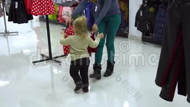 一个可爱的小女孩和她的母亲在一家精品店里家精品店。 妈妈和孩子在商店里挑选衣服