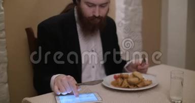一个留胡子的年轻人在餐馆吃饭，用平板电脑