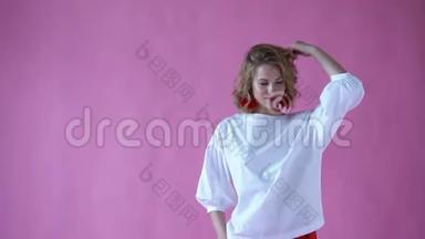 在一个粉色背景的摄影棚里，一个开朗、积极向上的金发女孩在为照相机摆姿势