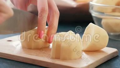 特写女人`她的手在木板上切土豆。