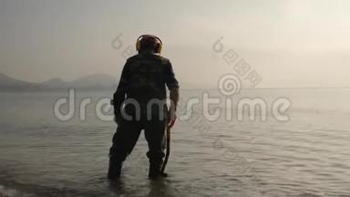 一个带着金属探测器的人正在海滩上寻找贵重物品