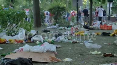 <strong>垃圾</strong>，包括塑料包装和瓶子，躺在公园的草地上，人们走过