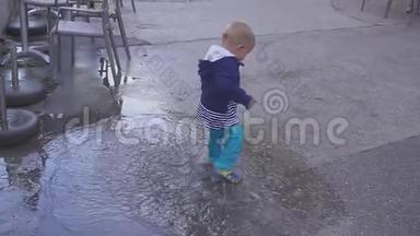 这个男孩在雨中的水坑里玩。 他在雨中快乐。 两岁的男孩在人行道上奔跑。 概念