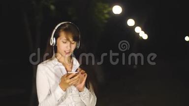 戴着耳机听歌、唱歌的女人通过触摸电话在城市公园里唱歌
