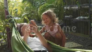 年轻女子在吊床上用智能手机和小女儿玩