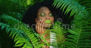 这位美丽的美国黑人妇女的近景，她涂着<strong>绿色</strong>的<strong>口红</strong>和眼影，抚摸着自己的脸颊。