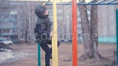 一个男孩爬在一座城市房子的院子里的猴栏上。 游戏和在游乐场散步。
