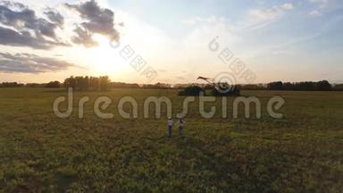 母亲和男孩带着风筝在绿色的田野上奔跑。 欢声笑语，喜庆的心情.. 秋天，日落