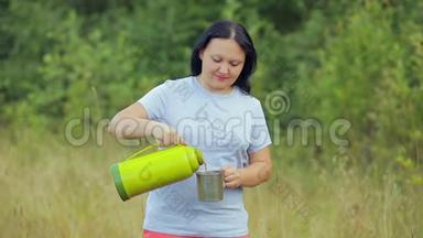 森林里的一个年轻女人把热水瓶里的热茶倒进杯子里。