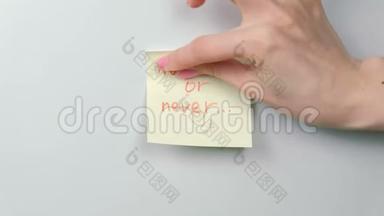 特写的女人`她的手贴着黄色的贴纸纸，上面写着现在或永远的话。