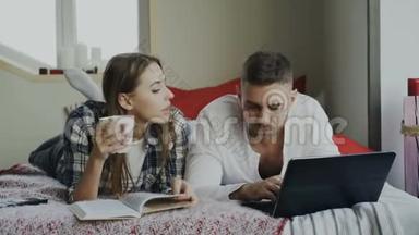 幸福夫妻在家休息。早上躺在床上看书用笔记本电脑的年轻男女
