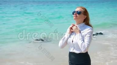 在海滩上戴太阳镜的女商人。 她在大海和太阳中快乐。 她解开衬衫扣子，呼吸着