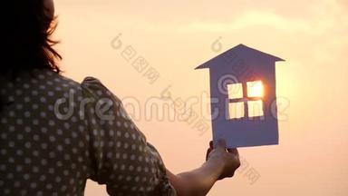 太阳落山时手里拿着纸房子的剪影。