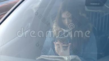 从汽车挡风玻璃上看到穿着蓝色<strong>羽绒服</strong>的年轻黑发女人看着电话。