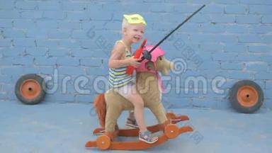 穿超级英雄面具的金发男孩坐在玩具摇马上。 儿童手持宝剑和信号号角，梦想着降临