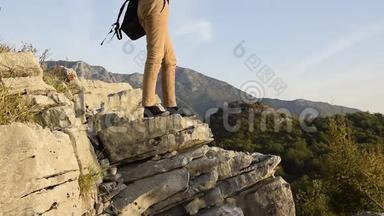 女徒步旅行者的双腿站在山崖的边缘，与美丽的山峰对峙