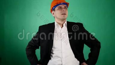 一个穿着橙色建筑头盔和西装的迷人男人看着相机。 一个年轻的工人用他的