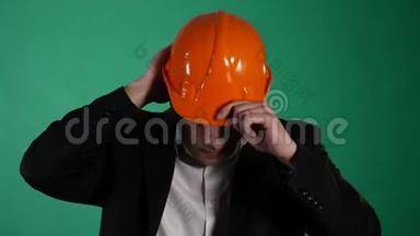 一个穿着橙色建筑头盔和西装的迷人男人看着相机。 一个年轻的工人用他的