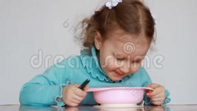 一个漂亮的小女孩坐在<strong>桌子</strong>旁，用盘子里的勺子吃食物。 这孩子仔细咀嚼。 <strong>早餐</strong>