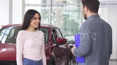 漂亮的幸福女人在收到汽车钥匙后与汽车经销商握手