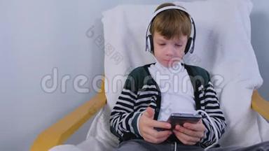 男孩正坐在家里的扶手椅上，用智能手机耳机听音乐。