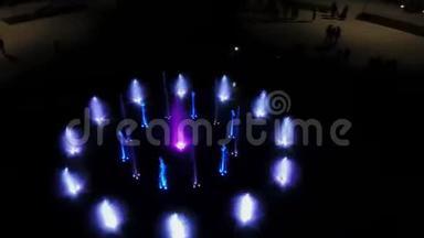 空中4k镜头舞蹈彩色喷泉在夜间。 彩色水射流在黑暗中用灯照明。