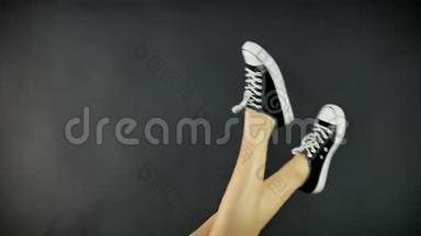 女腿穿经典<strong>黑白运动</strong>鞋.. 腿向上抬起，并从一边到另一边摇摆。 灰色，黑色