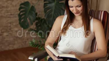 坐在椅子上看书的年轻漂亮女孩。一个迷人的女人在看书时笑。闭合。