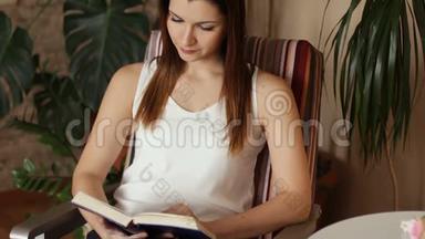 年轻漂亮的女孩坐在椅子上看书。 一个女人在业余时间聚精会神地看书。 快关门。